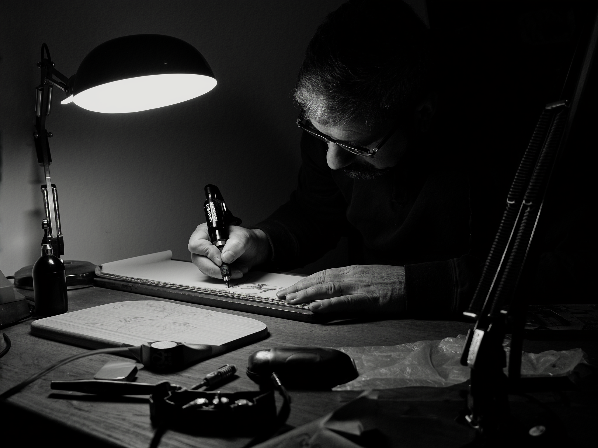 Tattoo-artiest buigt onder een werklamp over een schetsboek en tekent een ontwerp uit