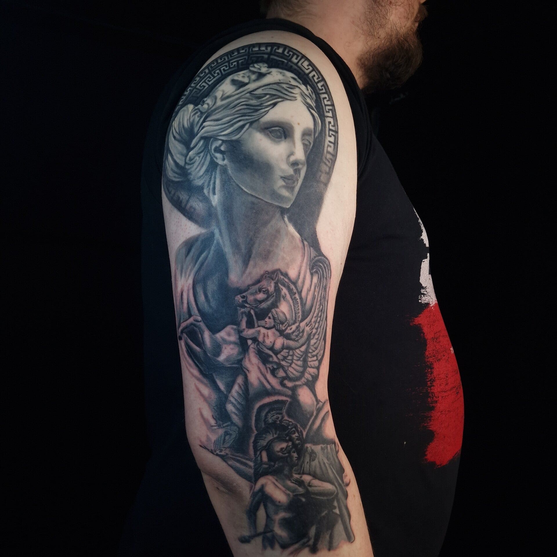 Bovenarm met een zwart-grijs tattoo van een klassiek vrouwenbeeld voor een Griekse meanderrand