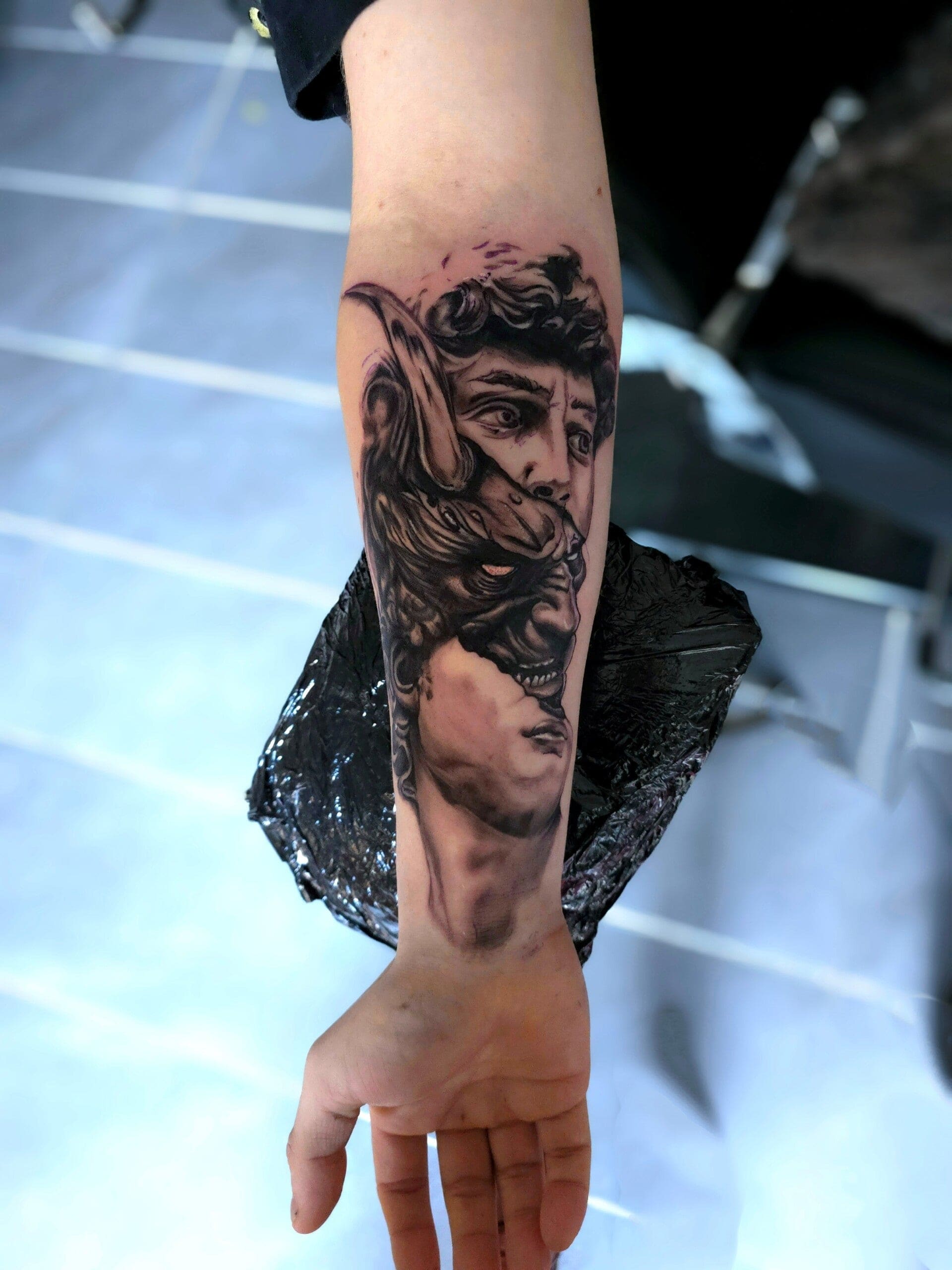 Onderarm met een zwart-grijs tattoo van een klassiek beeldhouwwerk dat openbreekt in een wolvenkop